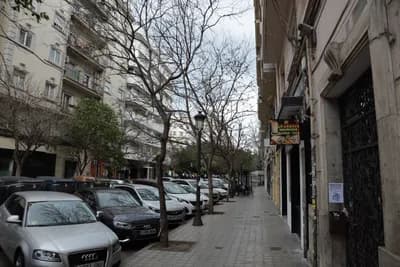 A street with parked cars and a sidewalk bordered by trees and buildings.