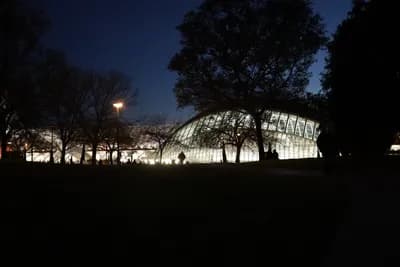 A modern, illuminated structure at dusk surrounded by trees and a dark sky.