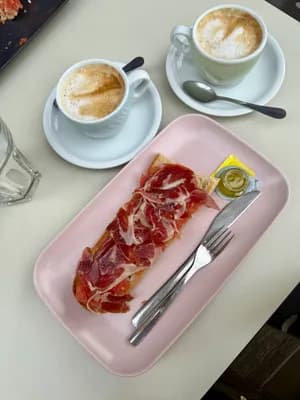 Jamón ibérico on a pink plate with coffee cups on a white table.