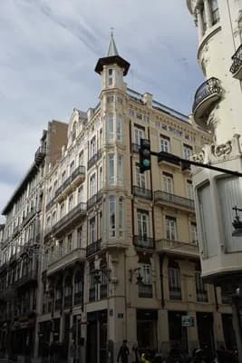 Historic building with balconies and a pointed tower at a street corner.