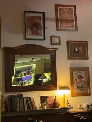 Opere d'arte incorniciate e uno specchio che riflette l'interno di un bar con una lampada accesa.