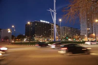 A modern sculpture and a lit hotel sign at night with a busy intersection in the foreground.