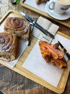 A wooden tray with a pastry, croissant, and utensils on a wooden table.