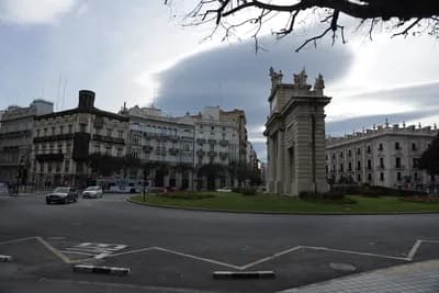 A city square with an arch and buildings under a cloudy sky.