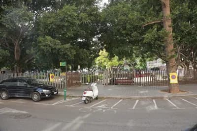 Scooter parked in designated parking space near fenced area with trees and car.