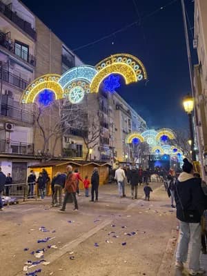 A street decorated with colorful lights and Christmas market stalls at night.