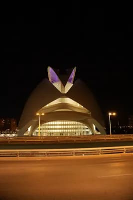 Modern architecture illuminated at night with a bridge in the foreground.