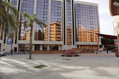 Modern building with reflective glass windows and palm trees in a paved plaza with a dome structure.