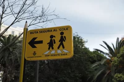 A yellow sign with a left arrow and figures of children walking, indicating a safe route to school.