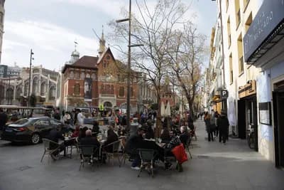 Outdoor dining scene with people at tables in a city square with historic buildings.