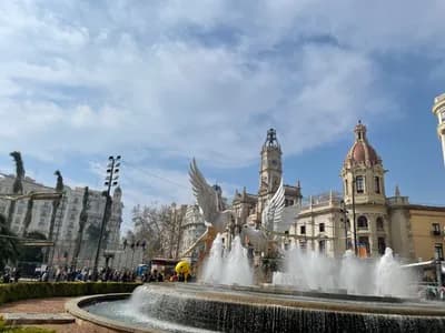 Fountain with winged statue in front of historic building with clock tower.
