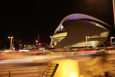 A futuristic building with curved architecture lit up at night, with light trails from vehicles in the foreground.