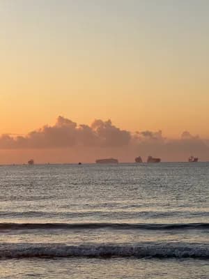 A tranquil sunset with calm waves and distant ships.