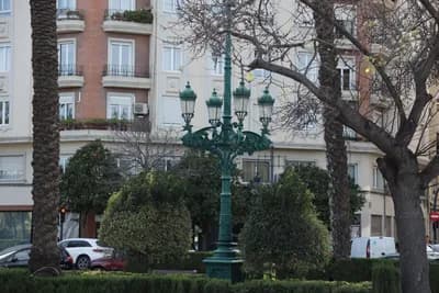 A green ornate street lamp with neatly trimmed bushes and trees in front of a residential building.