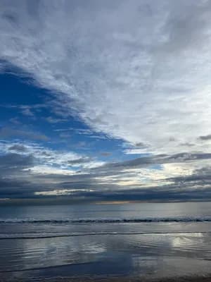 A tranquil beach with waves and a partly cloudy sky.