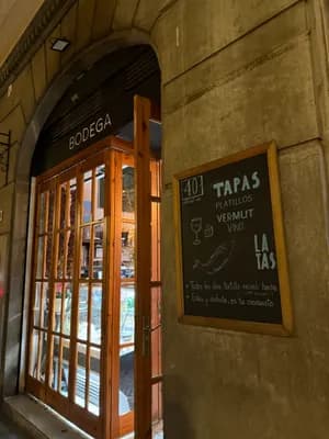 A wooden-framed door leading to a 'Bodega' with a chalkboard menu listing tapas and drinks.