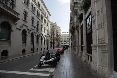 A street scene with parked scooters and historic architecture in Valencia, Spain.