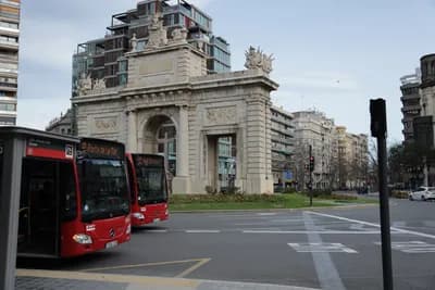 Red bus at a bus stop in front of an ornate archway in an urban setting