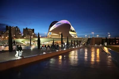 Modern architecture with illuminated bridge and people at dusk.