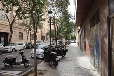 A street scene with parked scooters and cars, trees, and buildings.