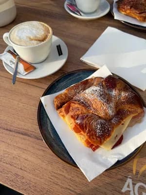 A croissant with powdered sugar and a cup of coffee on a wooden table.