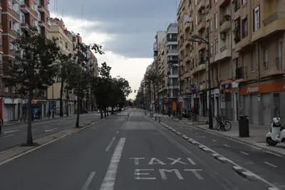 A quiet urban street with a taxi and EMT lane marked on the road, flanked by multi-story buildings and trees.
