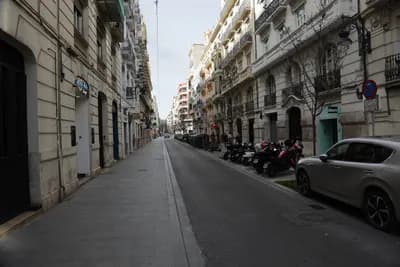 Quiet street with parked motorcycles and cars, ornate buildings, cloudy sky.