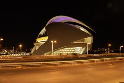 A modern, illuminated building at night with a bridge in the foreground.