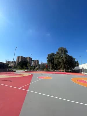 A basketball court with red and gray surfaces under a clear blue sky.