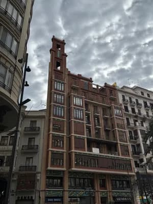 A red brick building with a tall tower and multiple balconies under a cloudy sky.