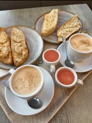 Table setting with cappuccino, tomato soup, and toasted bread.