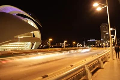 A modern building lit up at night with a bridge and streetlights in the foreground.