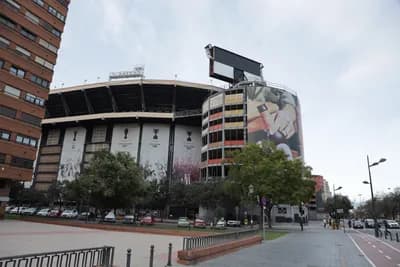 A stadium with a mural and parked cars beside a street.