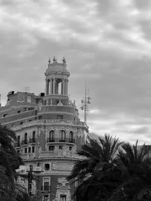 Ornate building with balconies and tower, palm trees, cloudy sky