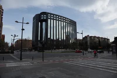 A modern building with a curved facade at an urban intersection with streetlights and a cyclist.