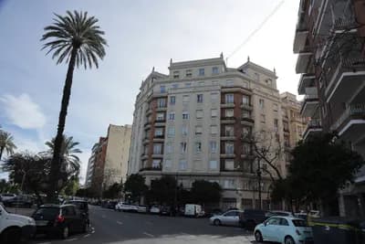 A street lined with palm trees and parked cars, featuring a multi-story building under a clear sky.