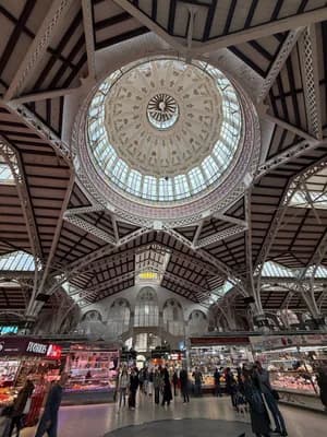Grand market interior with ornate dome and people shopping.
