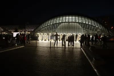 Illuminated 'VALENCIA' sign in front of a modern glass building at night.
