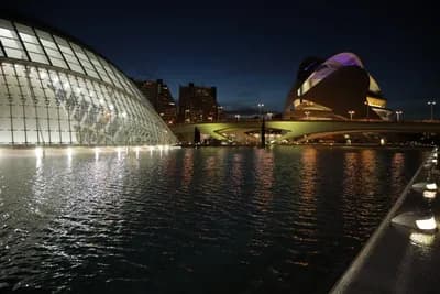 Modern architecture lit up at night, reflecting in water.