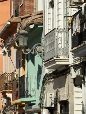 Colorful balconies with wrought iron railings and laundry hanging in a narrow street.