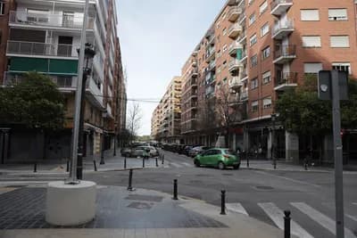 A street scene with residential buildings and parked cars under a cloudy sky.