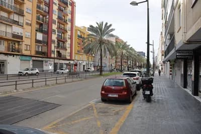 Parked cars and a scooter on a street with palm trees and residential buildings.