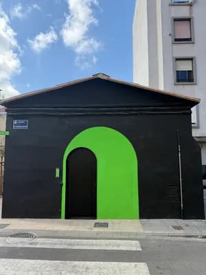 A small black building with a bright green door against a blue sky with scattered clouds.