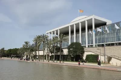 Modern building with glass facade and palm trees along a waterway.
