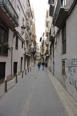 Narrow street with pedestrians and tall buildings in Valencia, Spain.