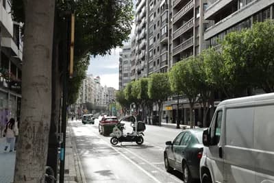 Urban street with trees, parked cars, and a scooter.