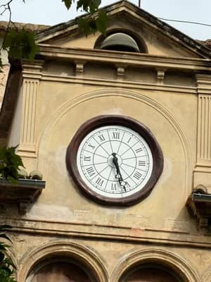 A large clock with Roman numerals on a building facade with arched windows and decorative columns.