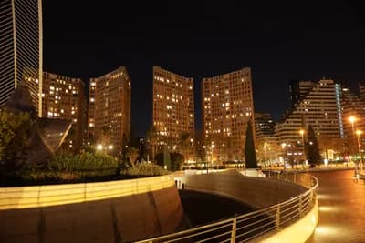 A nighttime view of a modern urban area with illuminated buildings and a curved walkway.