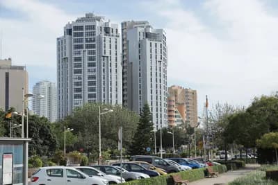 Modern high-rise buildings with parked cars and greenery in the foreground.