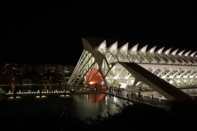Modern architecture at night with reflective water and illuminated structure.